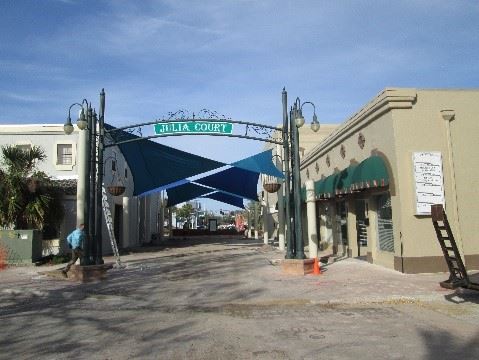 Photo of a courtyard between two buildings with shade sails hung across, and a large arch sign overhead.