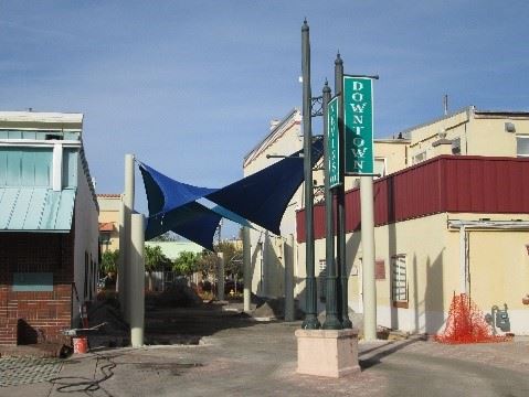 Photo of a courtyard between two buildings with shade sails hung overhead, and a blade sign in front.